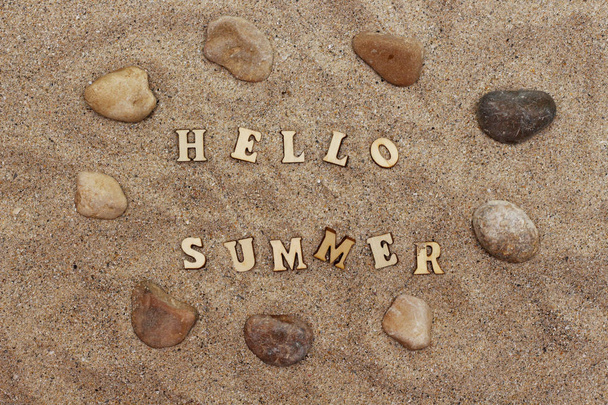 Деревянные буквы, образующие приветствие лето на песке и камнях вокруг песка
 - Фото, изображение
