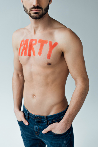 Cropped view of shirtless man with inscription on body standing with hands in pockets isolated on grey - Фото, изображение