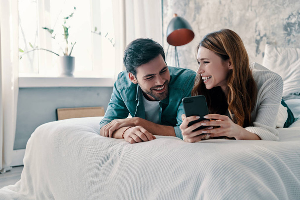 beautiful young couple using smart phone and smiling while spending time in bed at home    - Valokuva, kuva