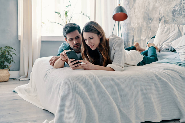 beautiful young couple using smart phone and smiling while spending time in bed at home    - Фото, зображення