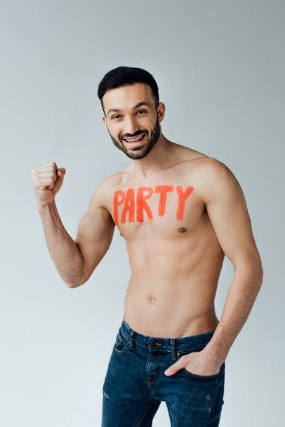Smiling shirtless man with inscription on body showing yes gesture on grey - Fotografie, Obrázek