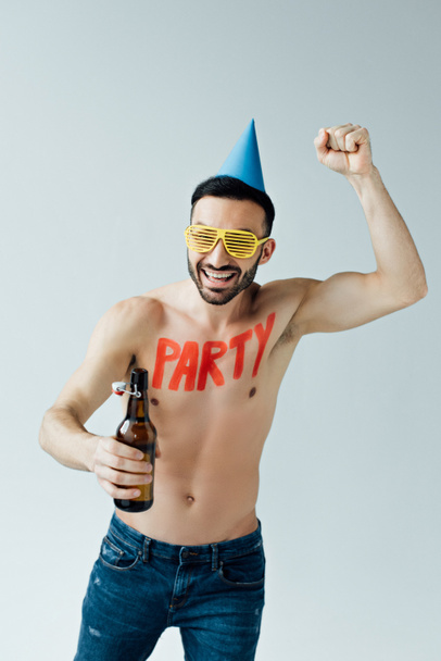 Γελώντας γυμνός άνθρωπος με καπέλο κόμμα κρατώντας μπύρα και δείχνοντας Ναι χειρονομία απομονωθεί σε γκρι - Φωτογραφία, εικόνα
