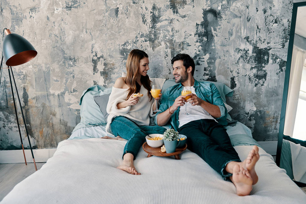 Perezosa mañana, Hermosa pareja joven desayunando con jugo de naranja mientras pasa tiempo en la cama en casa
               - Foto, Imagen