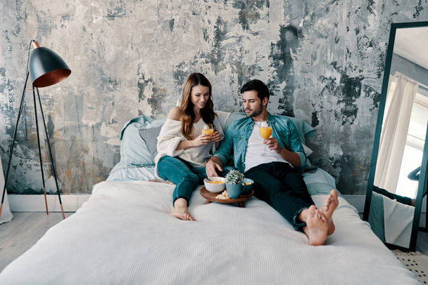 Mattina pigra, Bella giovane coppia che fa colazione con succo d'arancia mentre trascorre del tempo a letto a casa
               - Foto, immagini