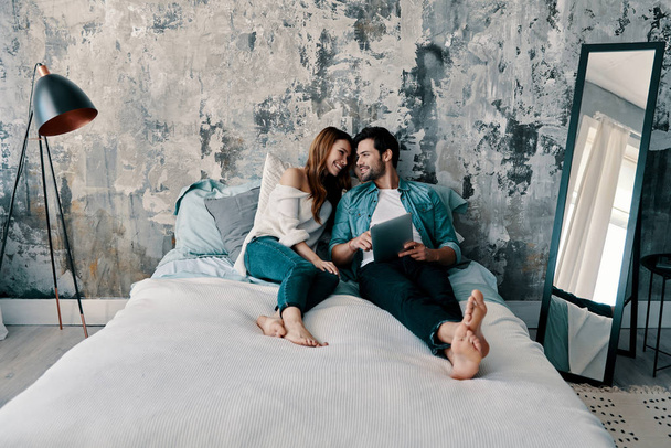 hermosa pareja joven usando tableta digital mientras pasa tiempo en la cama en casa
               - Foto, Imagen
