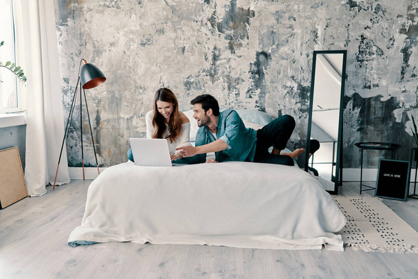 kaunis nuori pari tietokoneella viettäessään aikaa sängyssä kotona
             - Valokuva, kuva