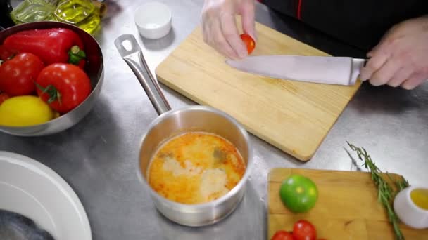 A chef working in the kitchen. Cutting the tomato in half and adding in the soup - Filmati, video