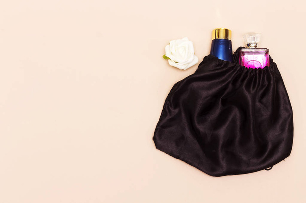 blue cream skin tube and pink perfume bottle in black bag and white rose flower - Foto, Imagem