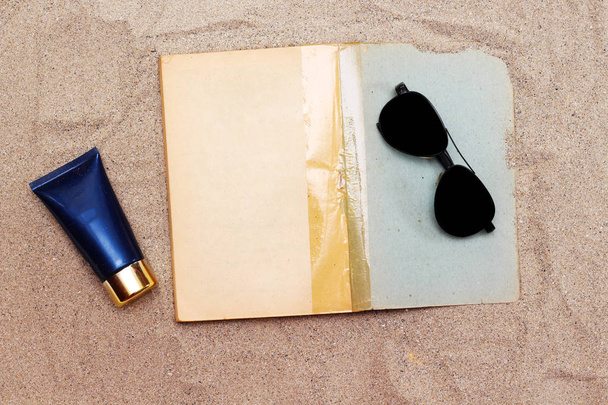 livro velho de papel vazio com tubo de creme azul e óculos escuros pretos acima da areia
 - Foto, Imagem