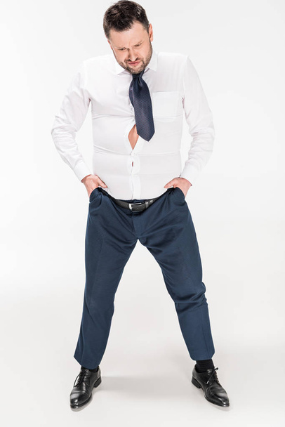 hombre con sobrepeso en apretado desgaste formal con las manos en bolsillos posando en blanco
 - Foto, imagen