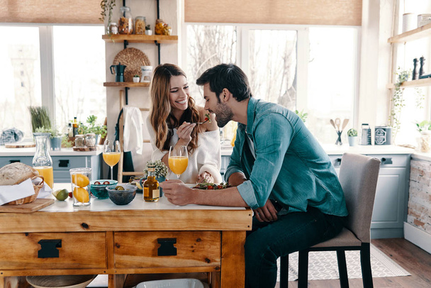 Beautiful young couple enjoying healthy breakfast while sitting in the kitchen at home          - Photo, Image