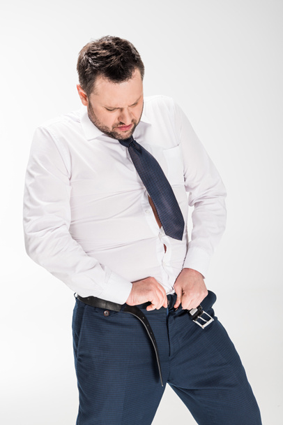 overweight man in formal wear putting on tight pants on white - Valokuva, kuva