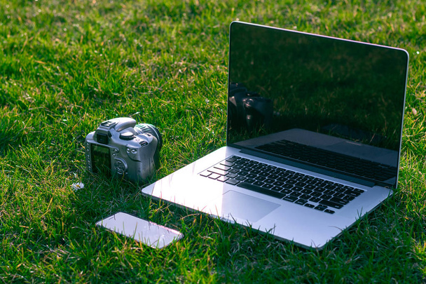 緑の草の上にスマートフォンと dslr カメラでノートパソコンのクローズアップショット - 写真・画像