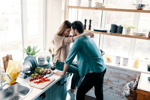 beautiful young couple bonding face to face while standing in the kitchen at home - Foto, immagini
