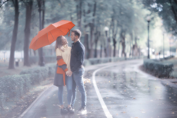 rain in the autumn park / young 25 years old couple man and woman walk under an umbrella in wet rainy weather, walk October lovers - Photo, image