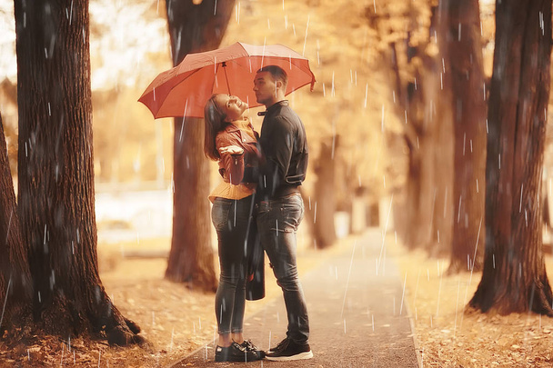 rain in the autumn park / young 25 years old couple man and woman walk under an umbrella in wet rainy weather, walk October lovers - Photo, image
