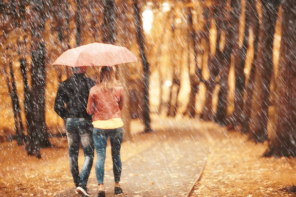 rain in the autumn park / young 25 years old couple man and woman walk under an umbrella in wet rainy weather, walk October lovers - Fotoğraf, Görsel