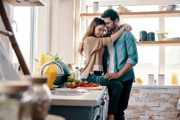 Beautiful young couple cooking dinner and drinking wine while standing in the kitchen at home - Foto, Imagem