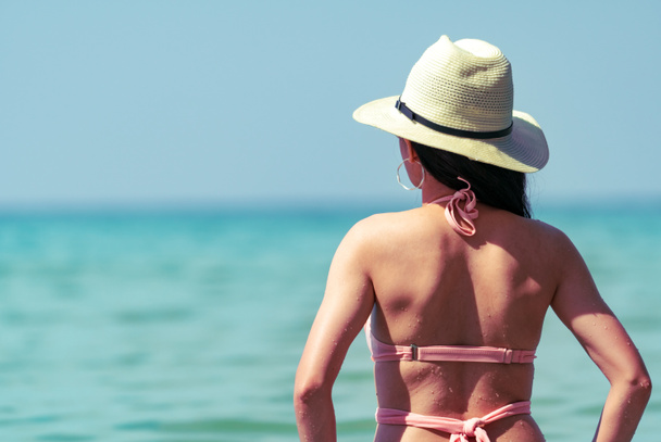 Achteraanzicht van de sexy jonge Aziatische vrouw slijtage roze bikini, strooien hoed en zonnebril ontspannen en geniet van vakantie in tropisch paradijs strand. Meisje in de zomer vakantie mode. Schoonheid sexy model. Zomer vibes. - Foto, afbeelding