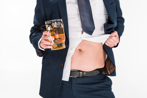 vista recortada del hombre con sobrepeso en el desgaste formal sosteniendo un vaso de cerveza y mostrando el vientre aislado en blanco
 - Foto, imagen