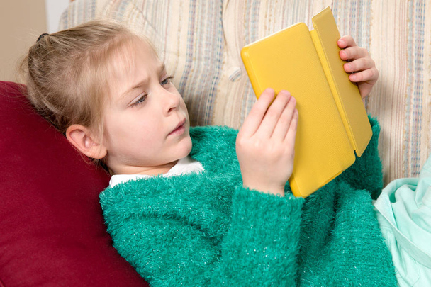 Young Girl Reading Tablet on the Sofa - 写真・画像