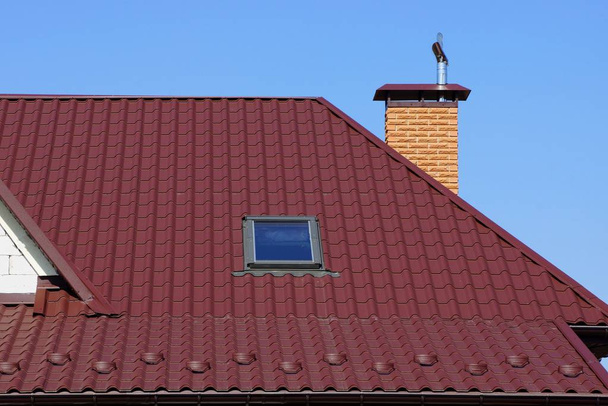 part of the house with red tiles on the roof with a window and a brick pipe against the sky - Photo, Image