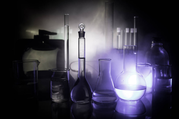 Pharmacy and chemistry theme. Test glass flask with solution in research laboratory. Science and medical background. Laboratory test tubes on dark toned background , science research equipment concept - Photo, Image