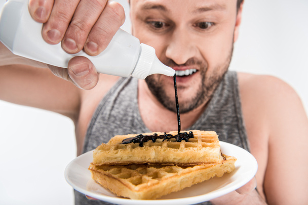 close up view of chubby man pouring chocolate syrup on waffles isolated on white - Photo, Image