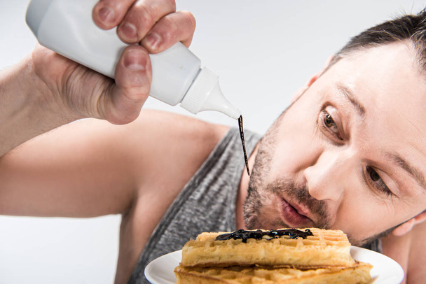 close up view of chubby man pouring chocolate syrup on waffles isolated on white - Fotografie, Obrázek