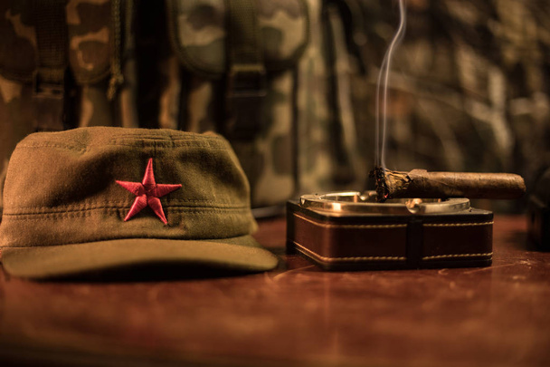 Close up van een Cubaanse sigaar en asbak op de houten tafel. Communistische dictator commandant tabel in donkere kamer. Generaal van het leger is werk tafelconcept. Illustraties decoratie - Foto, afbeelding