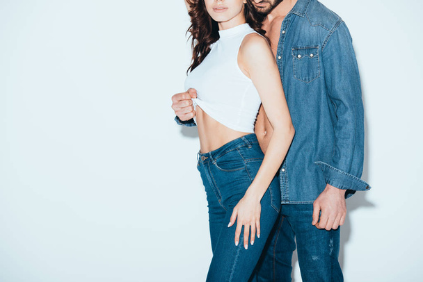 cropped view of man in jeans undressing girlfriend on grey - Foto, afbeelding