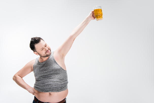 υπέρβαρο άνθρωπος στην κορυφή της δεξαμενής κρατώντας ποτήρι μπύρας με απλωμένο χέρι στο λευκό με χώρο αντιγραφής - Φωτογραφία, εικόνα