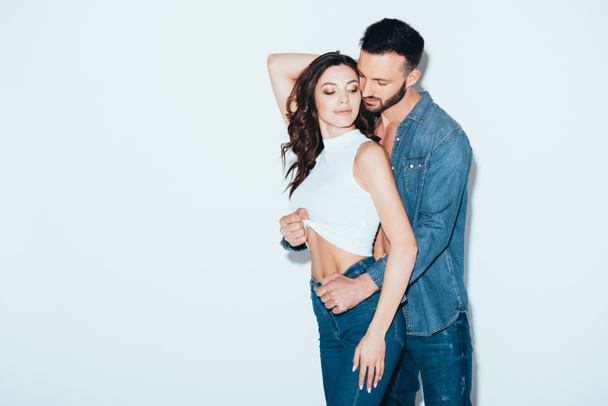 bearded man in jeans undressing girlfriend on grey - Fotografie, Obrázek