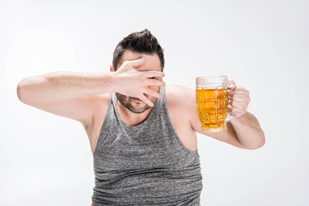l'uomo in sovrappeso che copre il viso con mano e tiene il bicchiere di birra su bianco
 - Foto, immagini