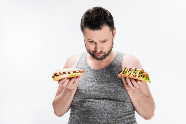 overweight man in tank top holding hot dogs isolated on white - Fotó, kép