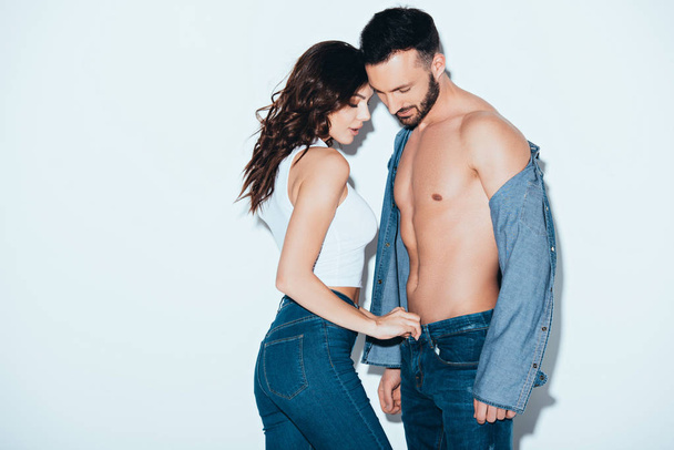 sensual young woman unzipping jeans on boyfriend on grey - Zdjęcie, obraz