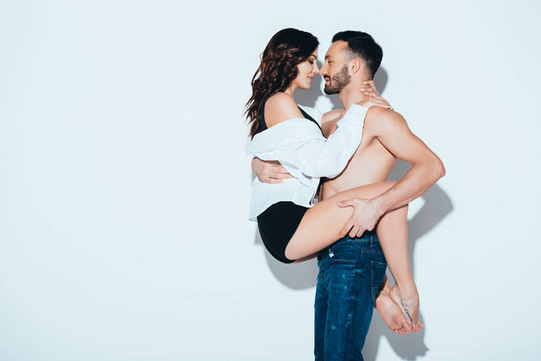 shirtless man in jeans holding girlfriend on grey - Фото, изображение