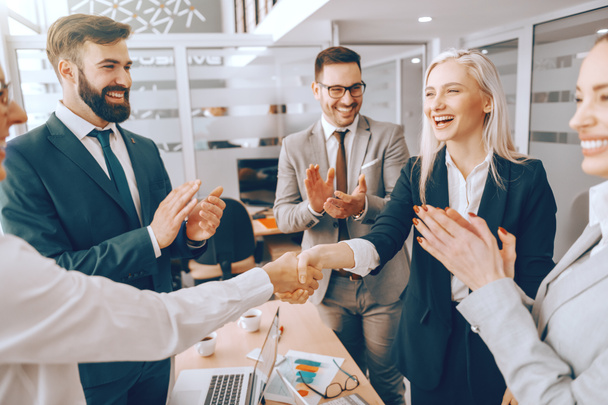 Business partners shaking hands while other colleagues clapping. Boardroom interior. Successful leaders have the courage to take action where others hesitate. - Фото, изображение