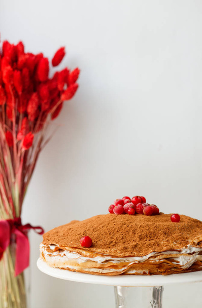 Gâteau de crêpe à la crème au beurre et cacao et groseille sur fond blanc avec des fleurs séchées
 - Photo, image