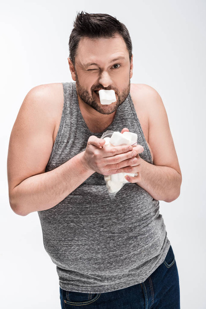 overweight man in grey tank top eating marshmallows isolated on white - 写真・画像