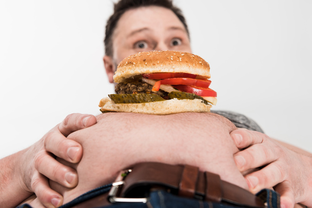 sorprendido hombre con sobrepeso hamburguesa en el vientre aislado en blanco
 - Foto, Imagen