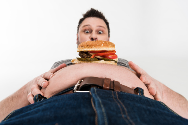 shocked overweight man with burger on belly isolated on white - Foto, immagini