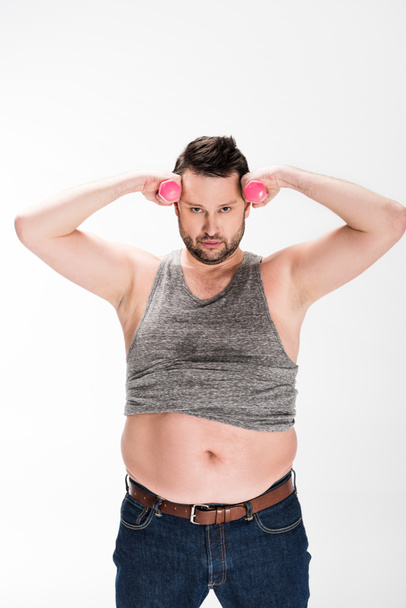 overgewicht man kijken naar camera tijdens het trainen met roze dumbbells geïsoleerd op wit - Foto, afbeelding