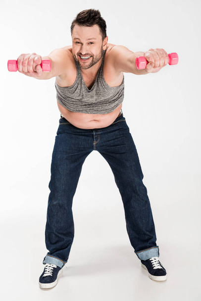 happy overweight man looking at camera while working out with pink dumbbells on white - Photo, Image