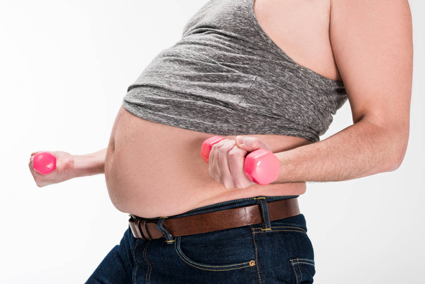 visão parcial do homem com excesso de peso mostrando barriga e trabalhando com halteres rosa isolados em branco
 - Foto, Imagem