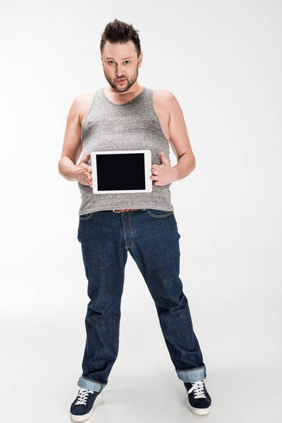 overweight man looking at camera and showing digital tablet with blank screen on white - Photo, Image
