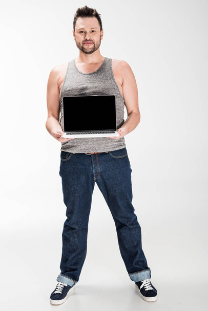 overweight man looking at camera and showing laptop with blank screen isolated on white - Foto, Imagen