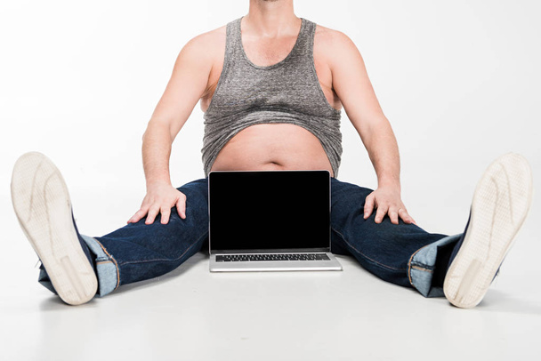 vista ritagliata di uomo in sovrappeso seduto vicino al computer portatile con schermo bianco su bianco
 - Foto, immagini