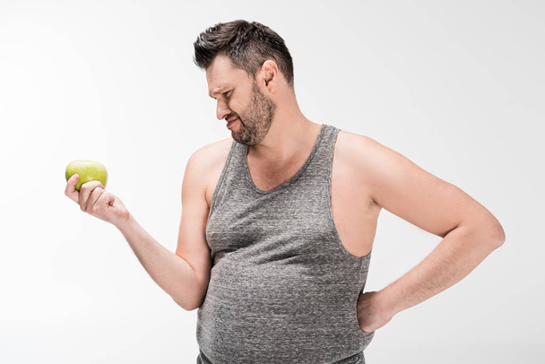 неудовлетворенный лишний вес человек держит зеленое яблоко изолированы на белом
 - Фото, изображение