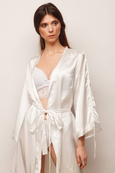 Sexy woman in white robe and white lingerie. Studio photo session - Foto, afbeelding